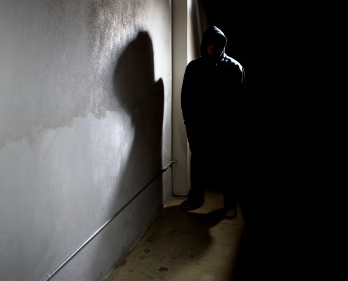 hooded criminal stalking in the shadows of a dark street alley